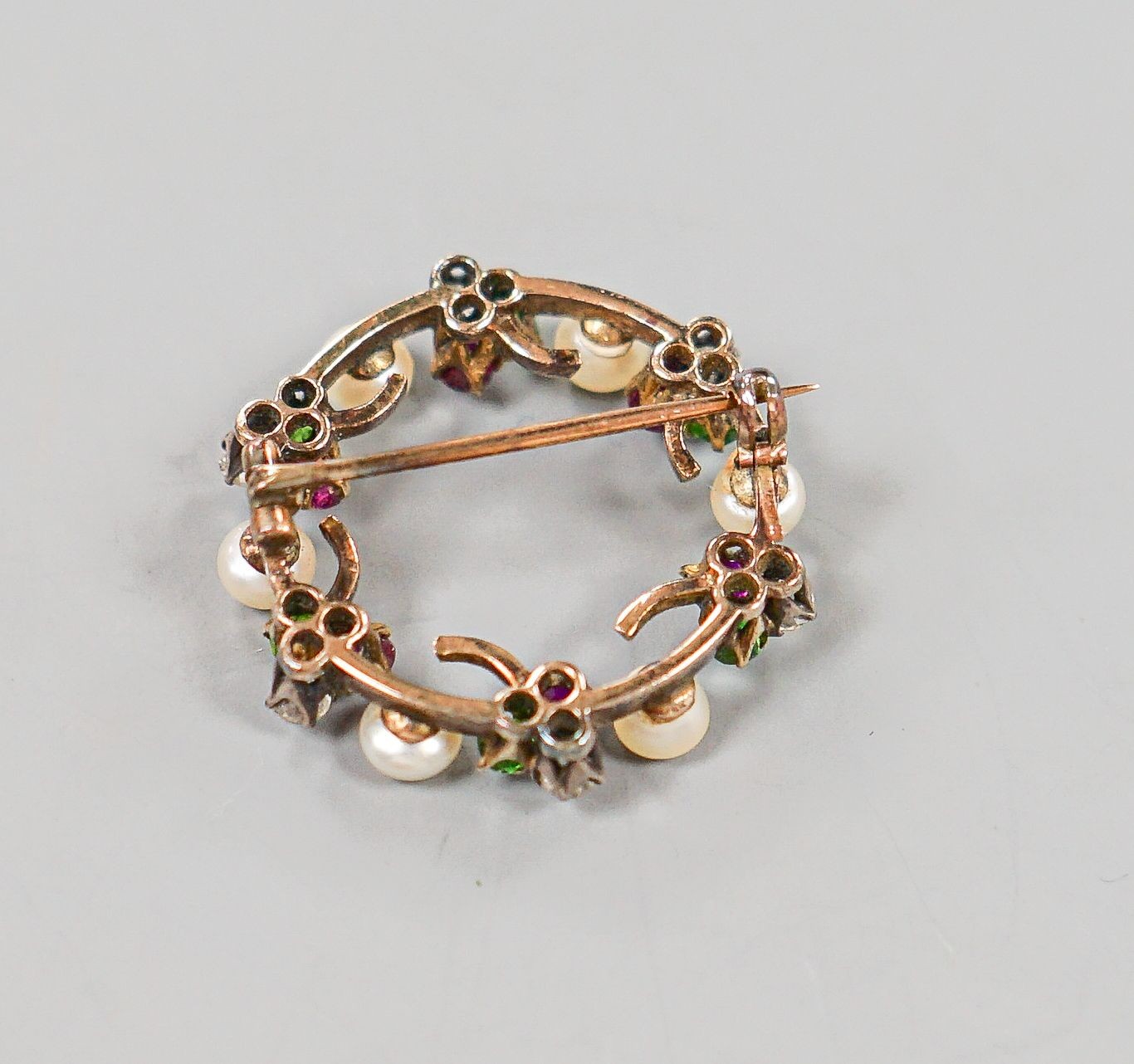 An early 20th century yellow metal, cultured pearl, ruby, garnet and diamond set openwork circular brooch, 25mm, gross weight 4.9 grams.